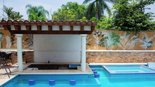 Una piscina con una pérgola, un mural y un muro de ladrillo.