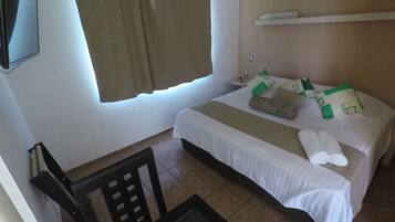Una habitación de hotel con cama, sillón, televisión y ventana con cortinas.