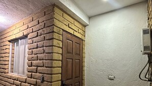 Fachada de ladrillo con puerta de madera, ventana con persiana y entrada empedrada en piedra.
