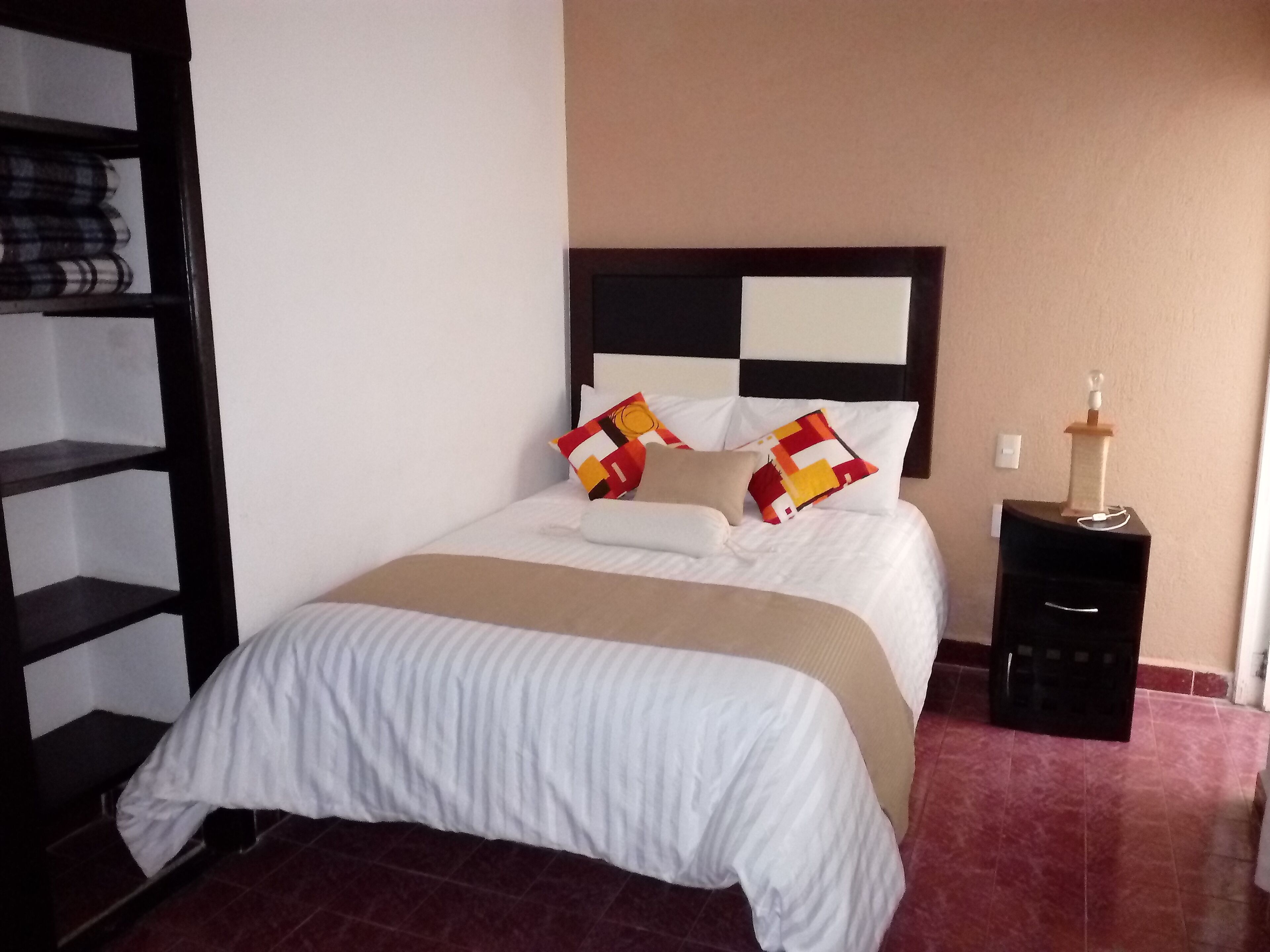 A neatly made bed with a white and beige bedspread, a black headboard, and two pillows with colorful patterns.