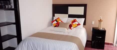 A neatly made bed with a white and beige bedspread, a black headboard, and two pillows with colorful patterns.