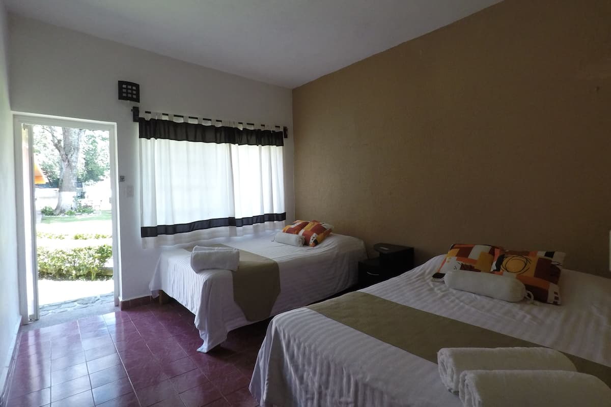 A hotel room with two beds, a small table, and a window with curtains.