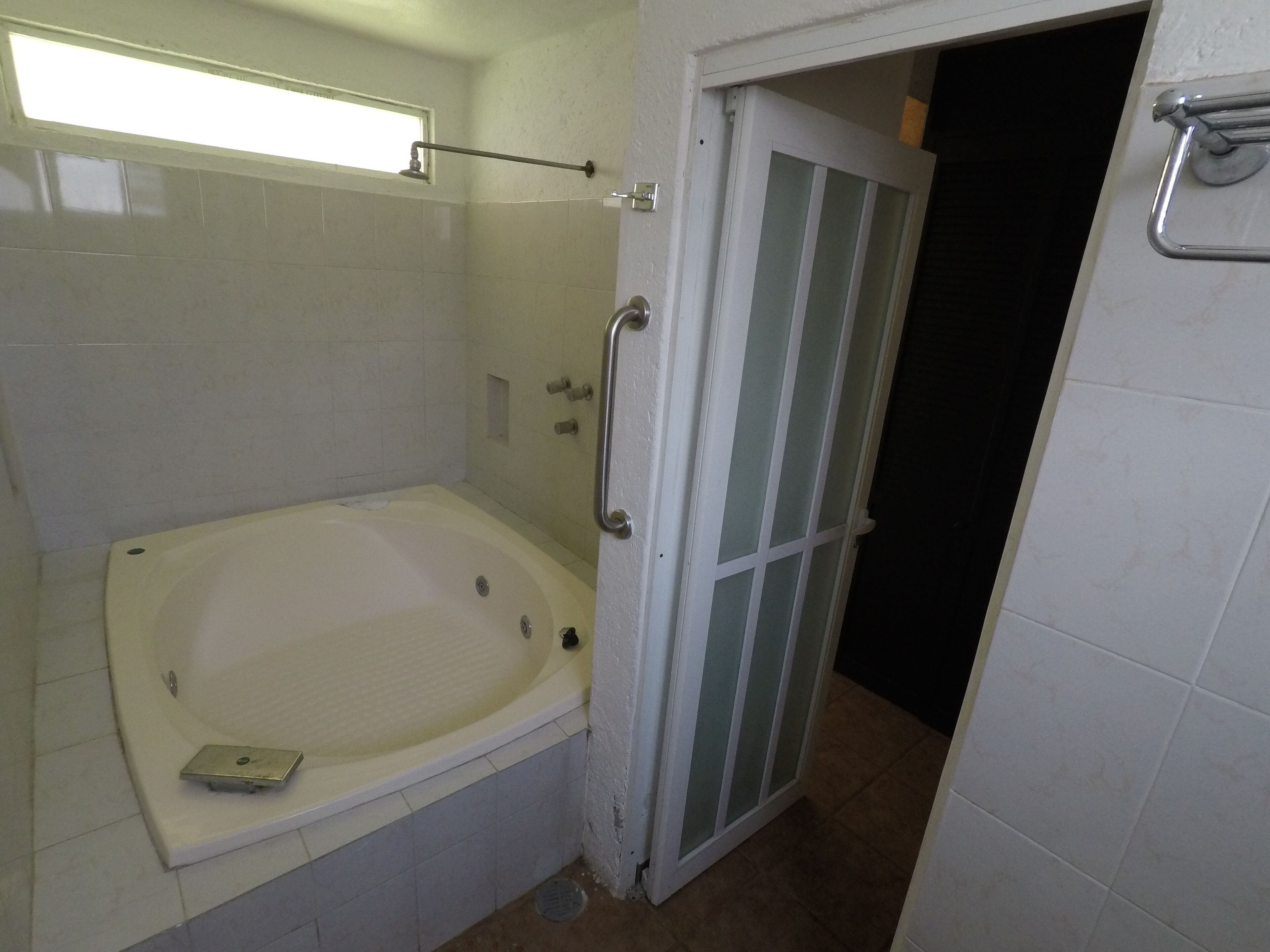 Une salle de bain avec une baignoire, une douche et une porte donnant sur une autre pièce.