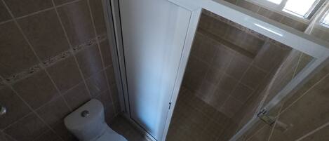 A bathroom with a toilet, shower, and a window.