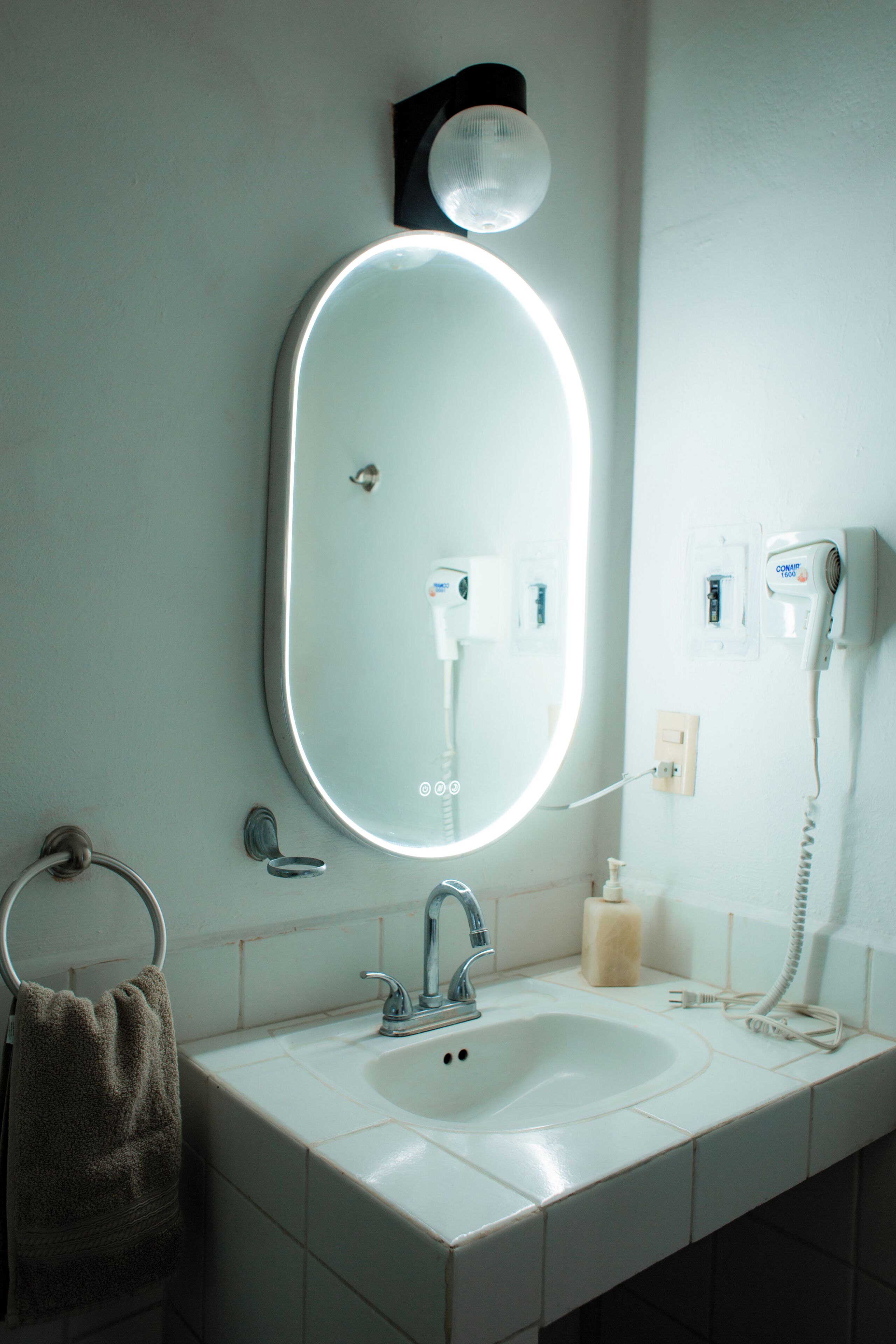 Casa de banho com uma pia branca, um espelho iluminado, um secador de cabelo e um porta-toalhas.