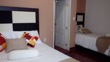 Habitación de hotel con dos camas, una con cabecera y la otra sin. Hay una puerta entre las camas y un espejo en la pared.
