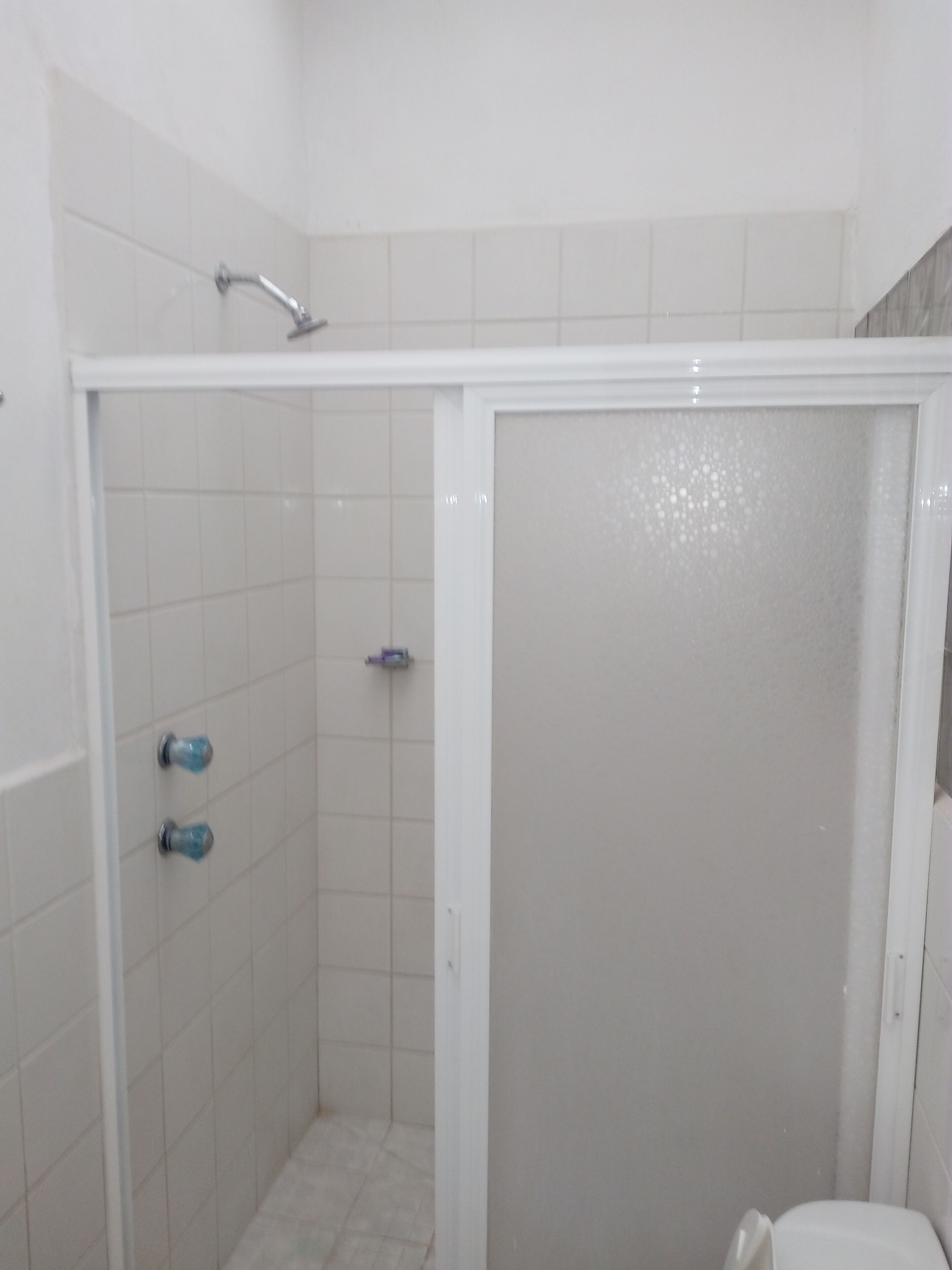 A shower enclosure with a frosted glass door, white tiled walls, and a showerhead.