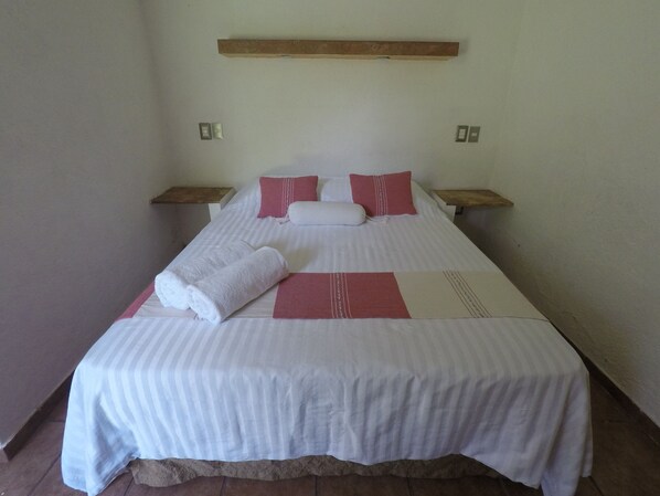 Una cama individual con ropa de cama blanca y detalles rojos, un cabecero de madera y dos mesitas de noche.