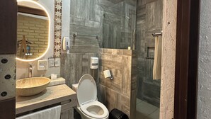 Un baño moderno con tocador de madera, un espejo redondo, inodoro y cabina de ducha de vidrio.