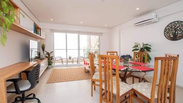 A modern dining area with a wooden table, chairs, and a red table runner. There are potted plants and a large window with a view.