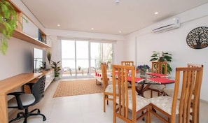 Un comedor moderno con una mesa de madera, sillas y un camino de mesa rojo. Hay plantas en macetas y un ventanal con vistas.