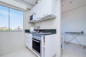 A compact kitchen with a stove, oven, microwave, and a window.