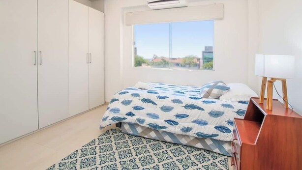Ein Schlafzimmer mit Bett, Fenster, Kleiderschrank und Klimaanlage.