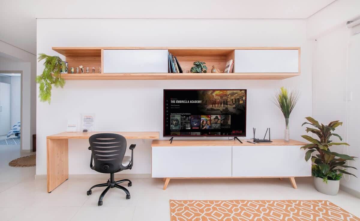 A modern office space with a desk, chair, television, shelves, and potted plants.