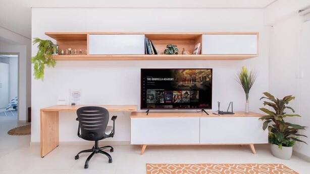 Un espacio de oficina moderno con escritorio, silla, televisor, estanterías y plantas en macetas.