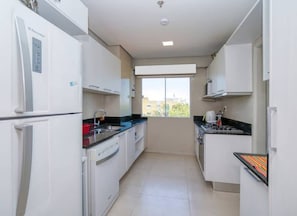 Une cuisine moderne avec des meubles blancs, un lave-vaisselle, une cuisinière et une fenêtre donnant sur les bâtiments environnants.