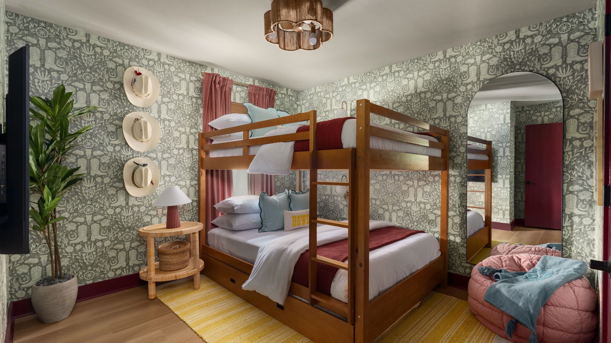 A bunk bed room with a television, a plant, a mirror, and patterned wallpaper.