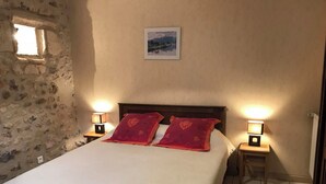Ein Bett mit zwei roten Kissen, zwei Nachttischlampen, einem gerahmten Bild an der Wand und einer Steinwand zur Linken.