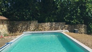 Ein rechteckiger Swimmingpool mit klarem Wasser, umgeben von einer Steinmauer und einer Rasenfläche.