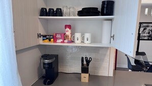 Una cocina con cafetera, juego de cuchillos y tazas de café en estantes.