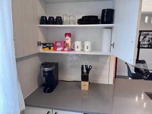 Een keuken met een koffiezetapparaat, een messenblok en koffiemokken op planken.