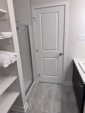 Een badkamer met een witte deur, een douchecabine en een wastafelgedeelte.