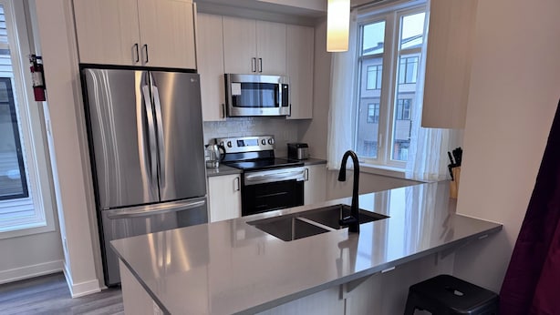 Una cocina moderna con electrodomésticos de acero inoxidable, una isla central con pileta y taburetes de bar.
