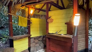 Una cocina rústica al aire libre con base de piedra, vigas de madera y pared amarilla.
