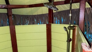 Ducha con cabezal de ducha y manguera de mano en un cuarto con vigas de madera y paredes amarillas.