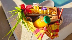 Una cesta de madera con jugo de naranja, un vaso, una servilleta y una flor junto a una piscina.