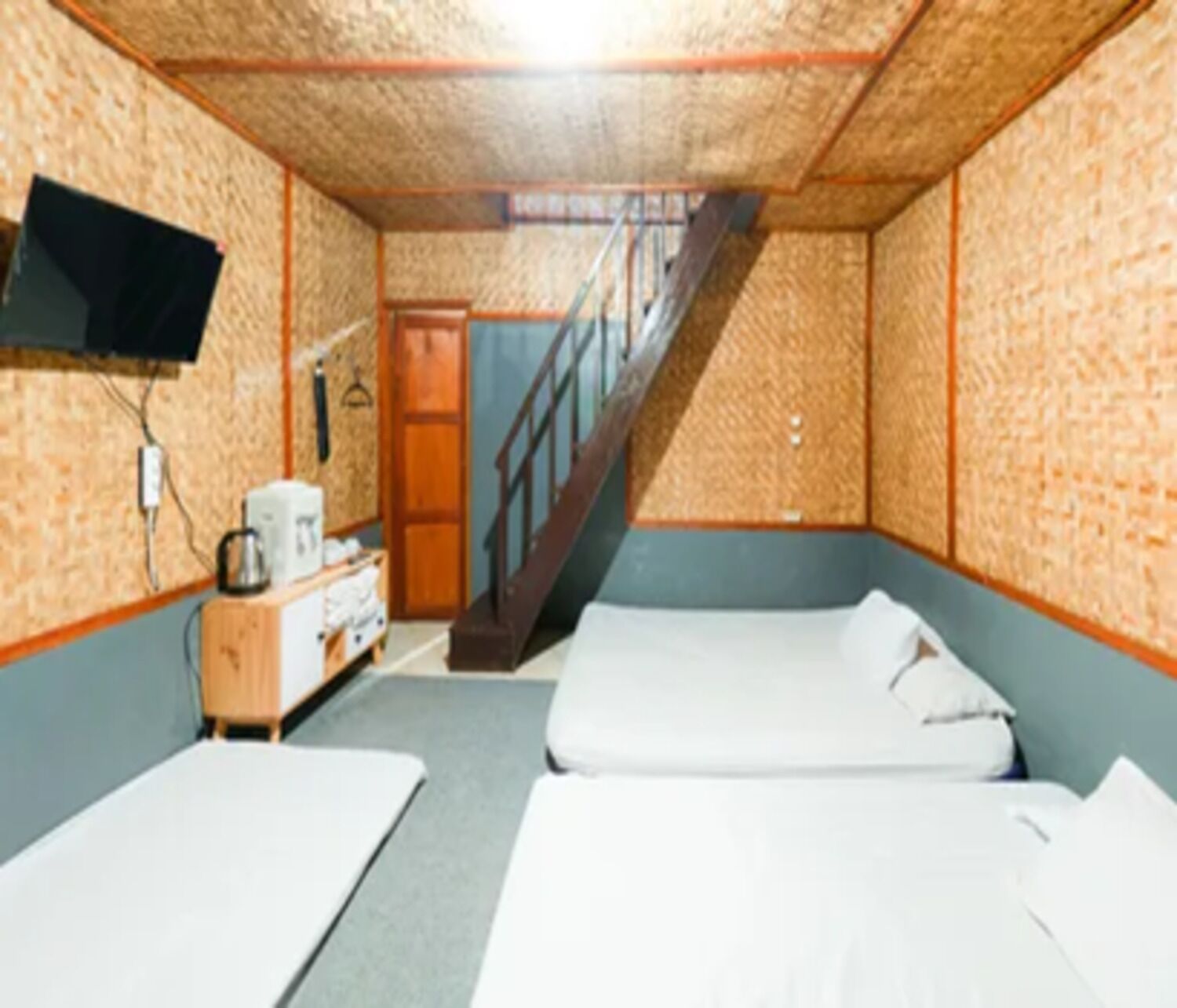 Ein Zimmer mit zwei Betten, einer Holzkommode, einem an der Wand montierten Fernseher und einer Treppe zu einer weiteren Ebene.