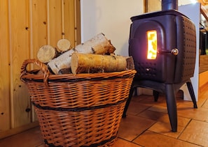 En korg av rotting, fylld med ved, står bredvid en vedeldad kamin.