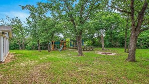 A playground with slides and climbing structures, surrounded by trees and a picnic table. - Blue Oasis (College Station)