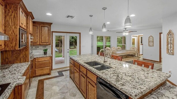 A modern kitchen with granite countertops, wooden cabinets, and a dining area with a table and chairs. - Blue Oasis (College Station)