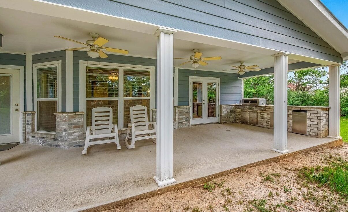 Une terrasse couverte avec deux chaises blanches, un barbecue et un ventilateur de plafond.