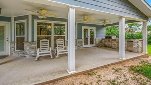 A covered patio with two white chairs, a grill, and a ceiling fan. - Blue Oasis (College Station)