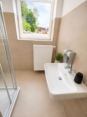 Ein Badezimmer mit Dusche, Waschbecken, Heizkörper und einem Fenster mit Blick ins Grüne.