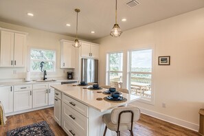 A kitchen with white cabinets, a large island, pendant lights, and a view of the outdoors. - Ozello Trail Sunrise Cottage (Crystal River)