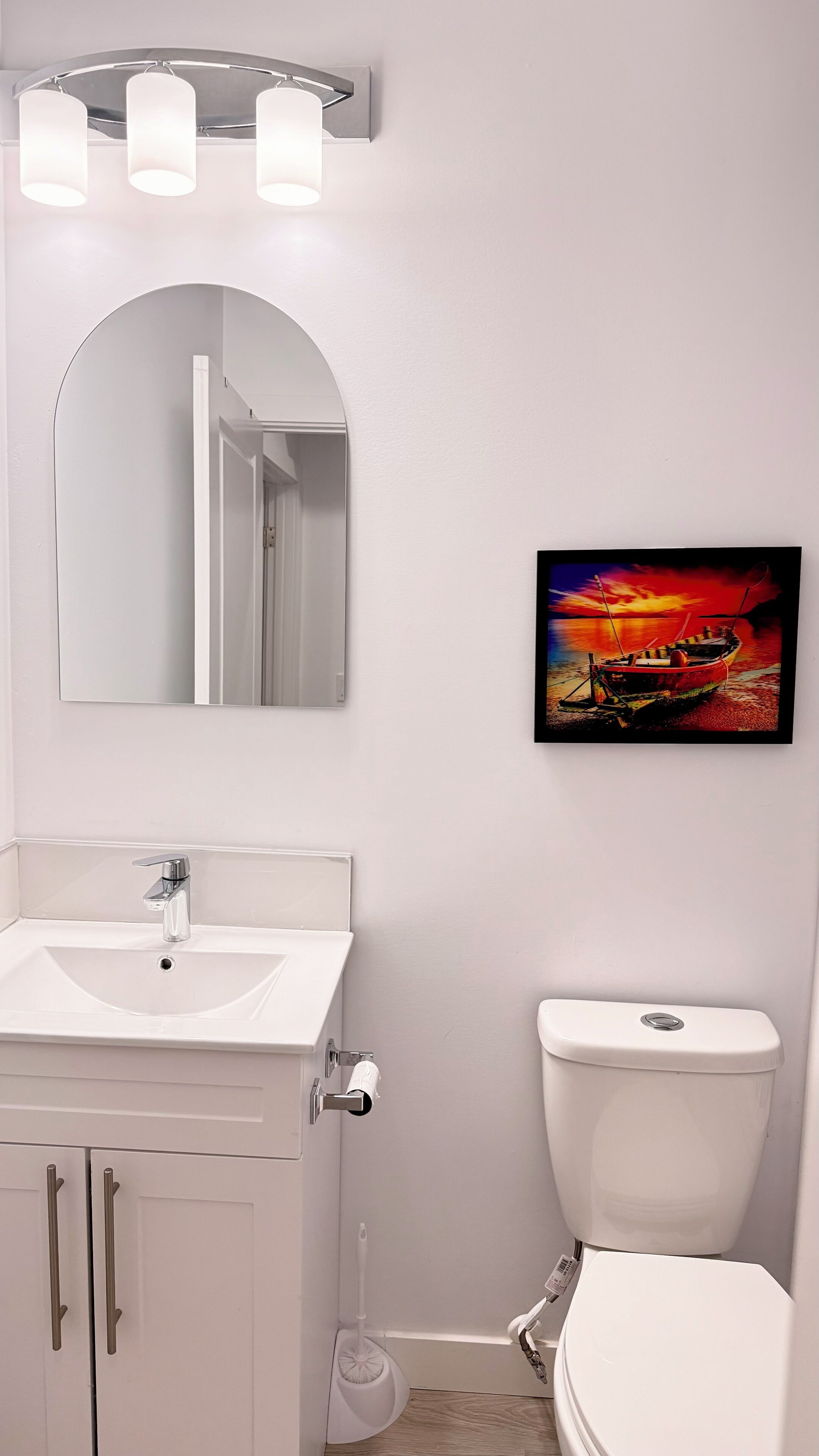 A bathroom with a white sink, mirror, and toilet. There is a painting of a sunset on the wall.