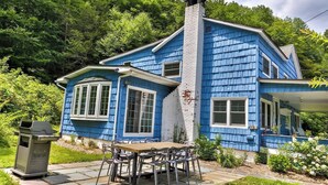 Ein blaues Haus mit Schornstein, Veranda und einer Terrasse mit Stühlen.
