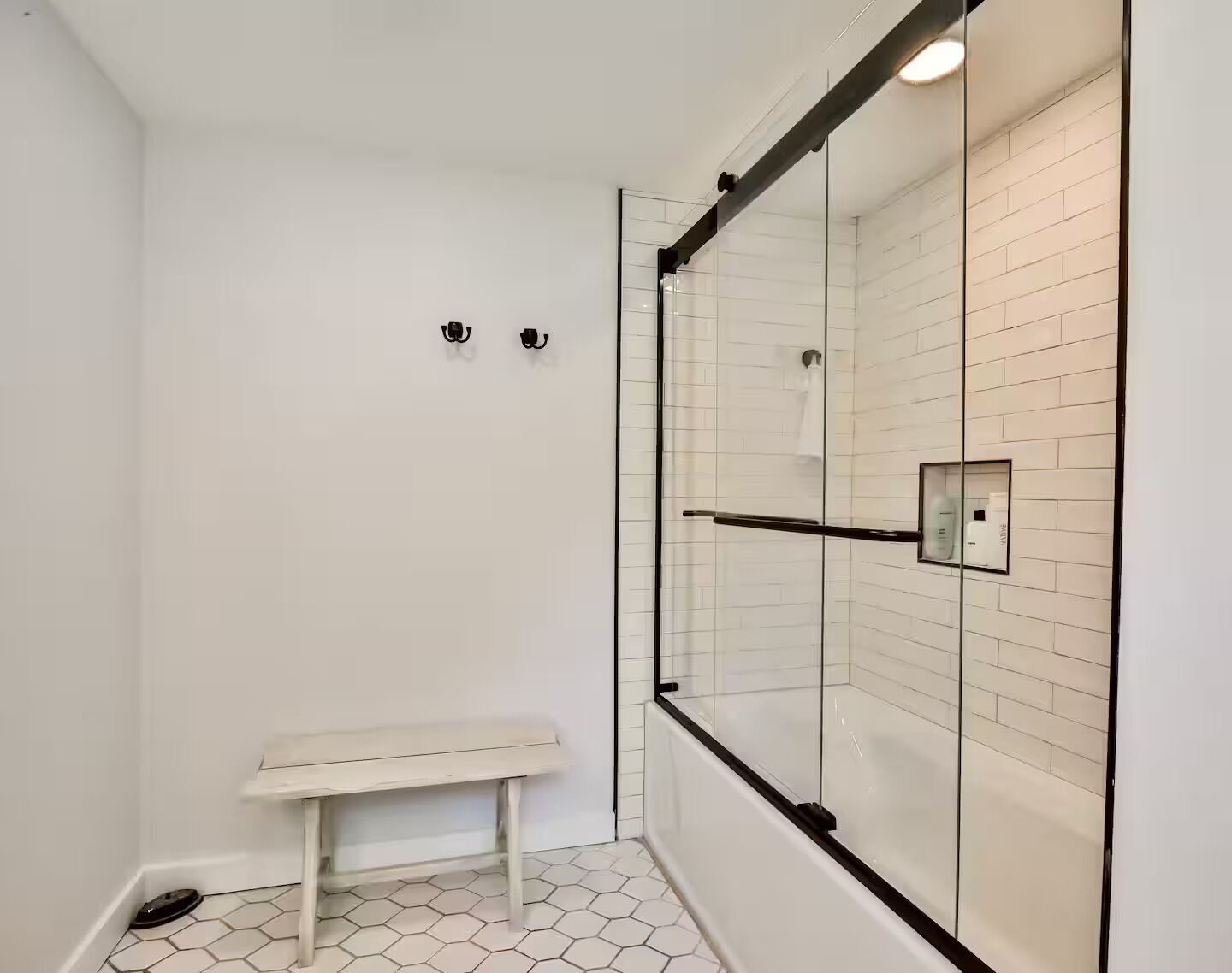 Une douche avec des portes en verre, un banc et un sol carrelé.