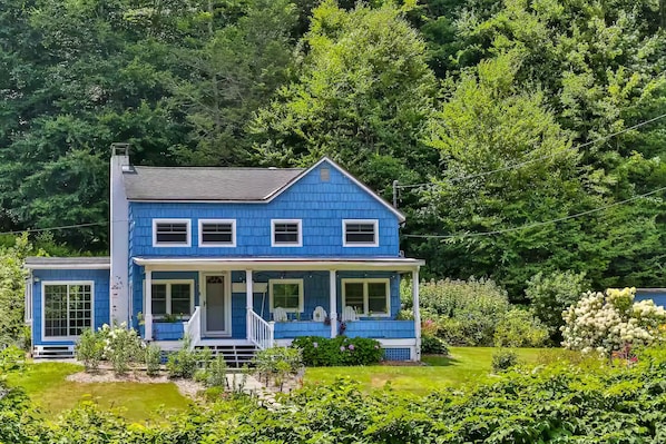 A two-story house with a porch, surrounded by lush greenery.