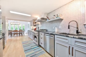Una cocina moderna con electrodomésticos de acero inoxidable, un salpicadero con estampado de espiga y un comedor con luz natural.