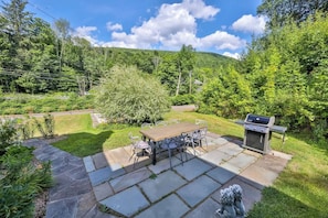 A patio with a grill, stone tiles, and a dining table with chairs.