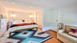 Ein Schlafzimmer mit einem Bett, einem Nachttisch, einem Standventilator, einem Sofa und einem gemusterten Teppich.