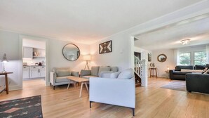 Ein geräumiger Wohnbereich mit einer Couch, einem Couchtisch und einem Esstisch. Im Hintergrund ist eine Küche zu sehen, und eine Treppe führt zu einer weiteren Ebene.