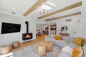 A modern living room with a fireplace, a sofa, and a dining area in the background. - Verbier Serenity Stay | Modern 3BDR | Pool & Spa (Mont-Tremblant)