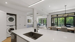Eine moderne Küche mit Spüle, ein Essbereich mit Tisch und Stühlen und ein Blick ins Freie durch große Fenster.