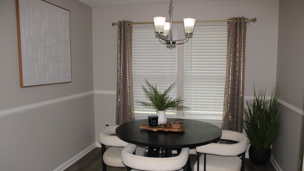 A dining area with a round table, six chairs, a chandelier, a potted plant, and a window with blinds. - Serene 1-bedroom house in charming Lithonia (Lithonia)