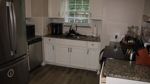 A kitchen with white cabinets, a stainless steel refrigerator, a coffee maker, and a window with blinds. - Serene 1-bedroom house in charming Lithonia (Lithonia)